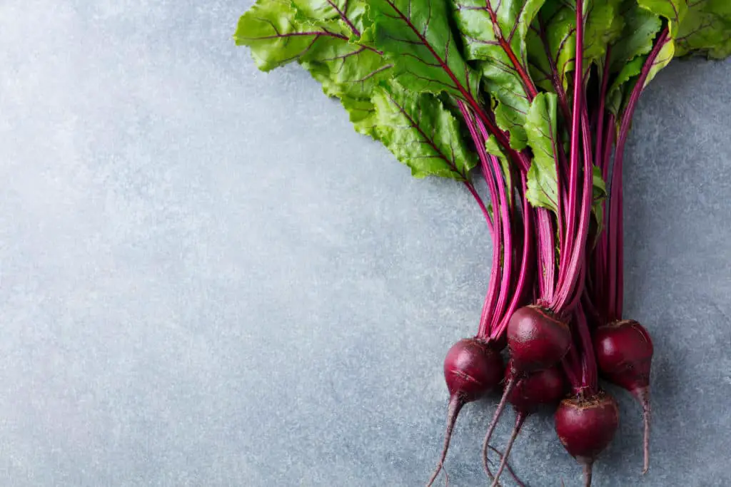 Bunch of beets with beet greens lying on a stone top