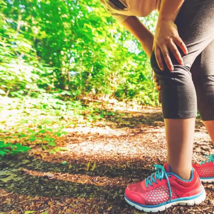 Woman in running shoes on a trail holding her knee in pain