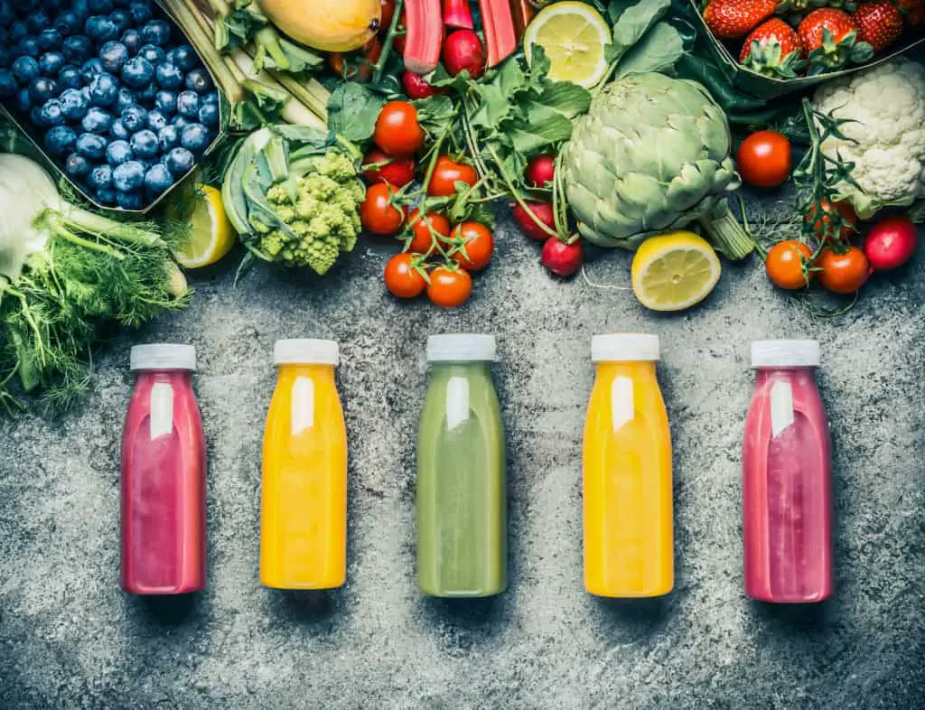 5 bottles of colorful fresh juice surrounded by fresh fruits and vegetables