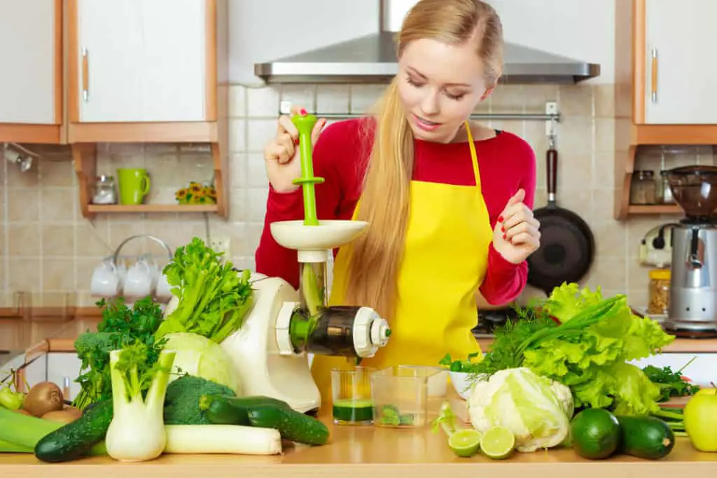 Woman making green juice with a masticating juicer, surrounded by vegetables