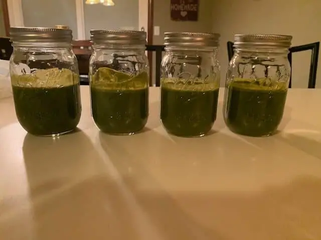 4 mason jars sitting on a white countertop filled with green juice