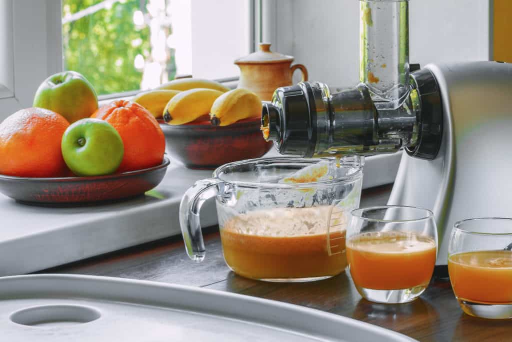 Horizontal masticating juicer on a wooden table making fresh carrot juice