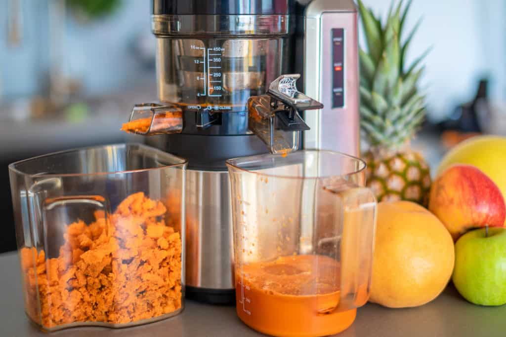 Vertical masticating juicer ejecting carrot juice from the juice port and ejecting carrot pulp from the pulp port