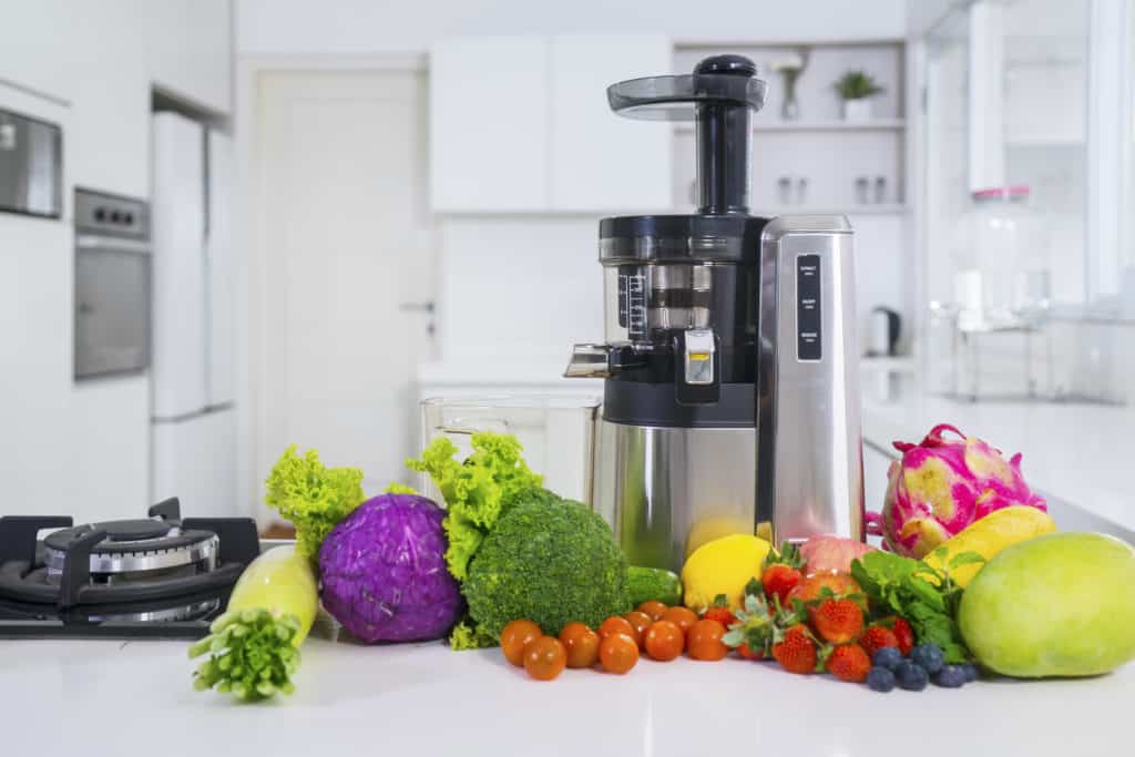 Vertical masticating juicer on counter surrounded by fruits and vegetables