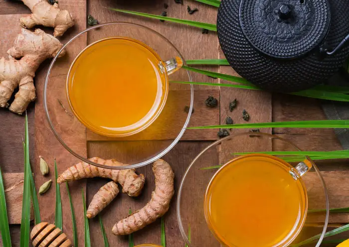 Turmeric and ginger root lying on a wooden table surrounded by turmeric tea